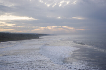Panoramic View of Wide Coastline at Sunset, Gentle Waves, Overcast Sky with Sun Rays, Serene Coastal Landscape in High Resolution
