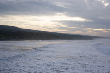 Fototapeta premium Panoramic View of Wide Coastline at Sunset, Gentle Waves, Overcast Sky with Sun Rays, Serene Coastal Landscape in High Resolution