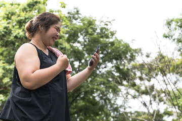 Asian fat fitness woman looking at smartphone during work out in public park