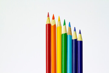 Rainbow coloured arrangement of sharpened pencils in a row on white background.