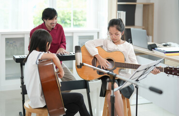 children concentrate on playing guitar with teacher in the classroom,adult help kid to learn music,concept of music studying,music education,art class,classical band