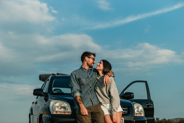 Young couple taking in the sunset after a road trip, their car parked nearby