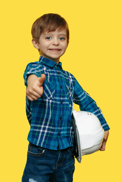 Smiling little kid boy engineer or architect in a protective helmet holding construction plan over yellow background.