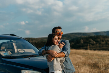 Man and woman standing side by side, appreciating the sunset next to their car