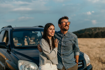 Man and woman standing side by side, appreciating the sunset next to their car