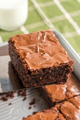 Freshly baked brownie with milk on a green tablecloth.