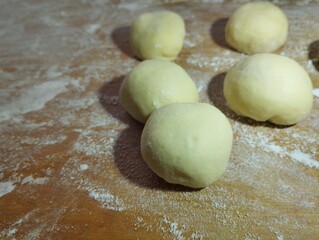 Preparation of festive donuts from dough and fruit filling. Small balls of dough on a wooden surface sprinkled with flour. Cooking theme.