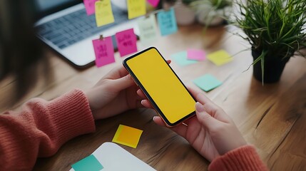 A person using a smartphone to set personal reminders and goals, with motivational sticky notes on the desk and a plant beside them