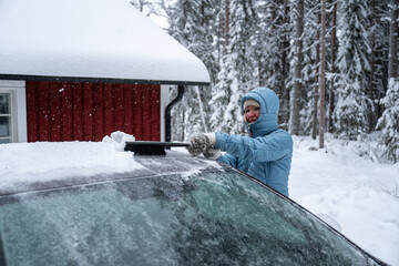 Woman remove her car from snow with brush. Car wash concept.
