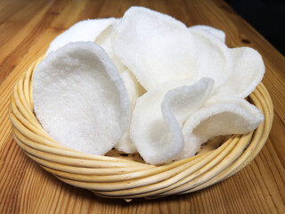 Closeup of crisp white deep fried prawn crackers, piled up in a wicker bowl, ready to eat.
