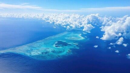 Aerial view of a vibrant turquoise lagoon surrounded by deep blue ocean and fluffy white clouds under a clear sky
