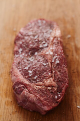 Raw ribeye steak spiced and ready to cook on oak board