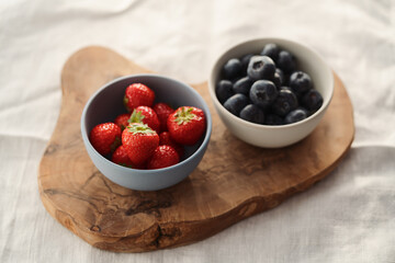 Two bowls with fresh blueberries and strawberries on woo dboard