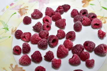 Frozen raspberries for making drinks lie on a plate.
