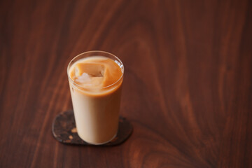 Ice coffee wih milk in tumbler glass on black walnut table
