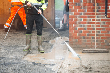 Worker cleaning a path surface with high-pressure water in a construction area during daylight hours