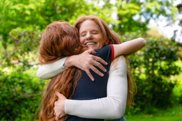 Fototapeta premium Two women share a warm hug in a sunny garden surrounded by lush greenery