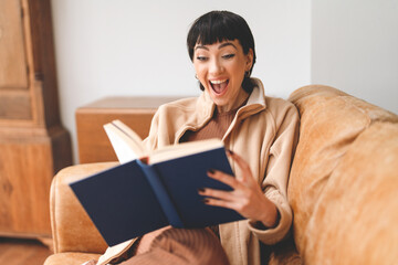Naklejka premium Young woman enjoys reading a book on a cozy couch in a modern living room