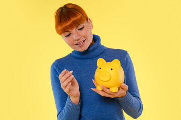 Young woman with orange hair saves coins in a bright yellow piggy bank