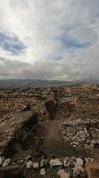 Ruins of the ancient fortress at Tel Hazor, a UNESCO World Heritage Site in northern Israel's Galilee, set against dramatic cloudy skies and lush natural green surroundings.