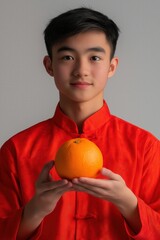 Asian Man in Red Traditional Attire Holding an Orange