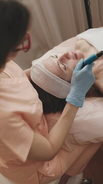 Professional cosmetologist conducting microneedling treatment with a specialized pen on a client's skin in a clinical setting.