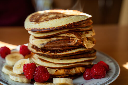 A stack of golden-brown pancakes topped with fresh raspberries and banana slices. The image evokes a sense of warmth and a delicious breakfast.