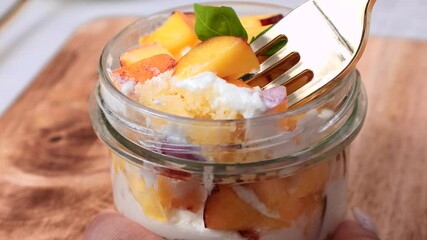 Homemade peach shortcake trifle cup with fresh peaches and whipped cream taking with a fork for eating close up
