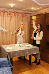 A girl and her younger brother decorate a room and a festive table for a birthday celebration. Soft lighting.
