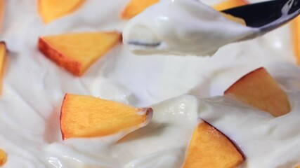 White yogurt with fresh peach pieces taking by a spoon close up