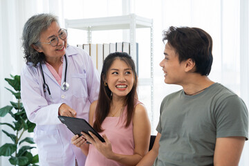 Senior female obstetrician consulting pregnant woman and her husband in medical clinic or hospital planning pregnancy. Visit to hospital, planning pregnancy, happy patients, trust and respect concept