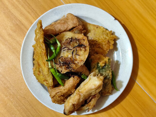 Gorengan, a traditional Indonesian street food consisting of tahu brontak, fried banana, bakwan, tempe mendoan, etc. Served with green chili.