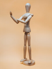A wooden mannequin of a man bends one arm at the elbow with his fist up in the form of an obscene...