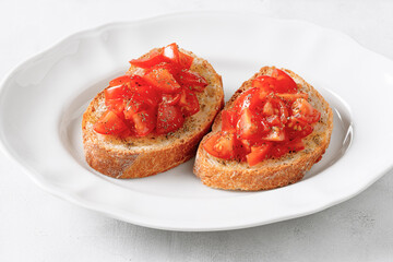 Two italian bruschettas with tomato and oregano on a white plate.