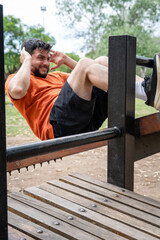 Hombre concentrado en su entrenamiento, haciendo abdominales en una tabla pública en el parque