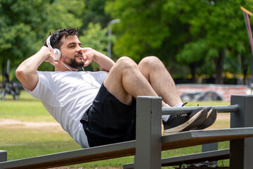 Hombre sonriente entrenando en el parque, haciendo abdominales mientras escucha música