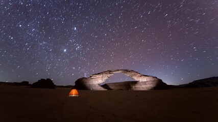 Time lapse of stars motion in rainbow arch night camping tent, with beautiful rock Al ula, Madinah,  Saudi Arabia