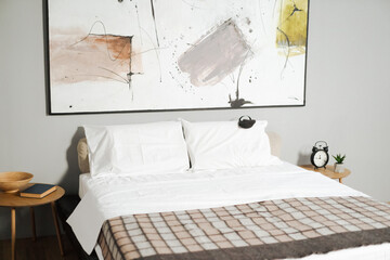 Bed with a white comforter and a brown and tan blanket. A clock is on a table next to the bed