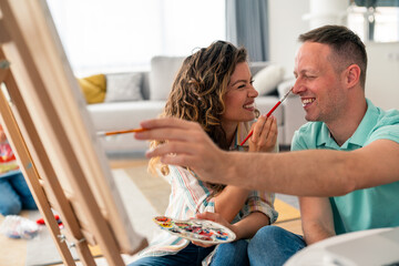 Mid adult Caucasian couple shares laughter while painting with colorful palette in casual attire...