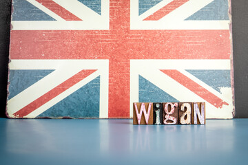 Obraz premium WIGAN. Urban Area in Great Britain. Flag and alphabet letters on wooden texture background