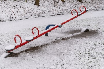 Red seesaw covered with snow in a playground during winter