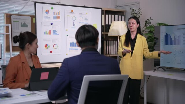 Professional Asian businesswoman presenting marketing data, explaining strategic insights with colleagues during collaborative team meeting in modern corporate boardroom
