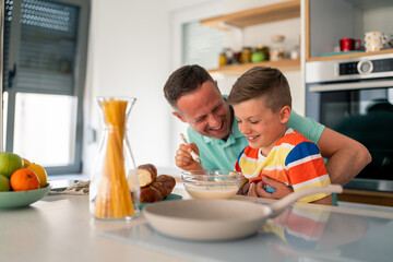 Caucasian father guides young son in mixing ingredients while preparing homemade meal in...