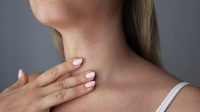Young blonde woman touching her neck with her hand on a dark grey background. Lines on the female neck. Wrinkles, age-related changes, rings of Venus, creases, goosebumps