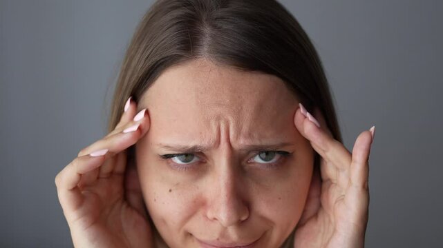 Young caucasian woman touching the forehead showing active facial expressions on her face by raising and lowering her eyebrows on a dark grey background. Wrinkling the forehead. Skin care. Close up