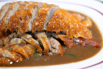 Close up of a plate of sliced roasted duck with crispy skin and juicy meat with sauces.