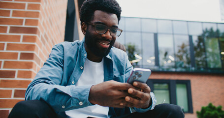 Attractive African American male smiling while using his smartphone. Picking up unexpected phone...