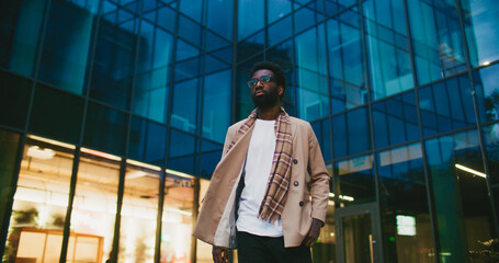 Stylish African American man confidently walking away from modern tall building. Woman passing by...