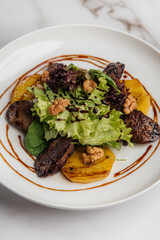 Warm salad featuring roasted veal, caramelized pear, fresh lettuce, and crunchy nuts drizzled with balsamic sauce on a white plate atop a marble table. Restaurant or cafe menu, cookbook recipe