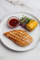 Delicious and healthy grilled chicken breast served with corn, red onion, microgreens, and barbecue sauce, representing a balanced and flavorful meal. Restaurant or cafe menu, cookbook recipe